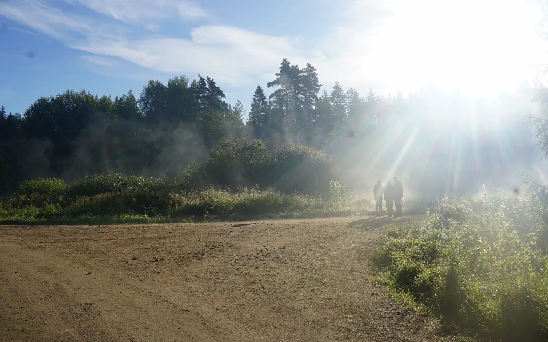 Three people are standing in the thick morning fog. They are illuminated by the sun.