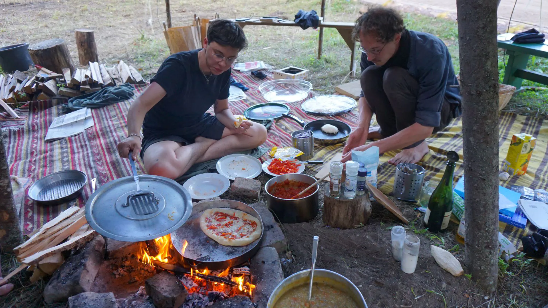 Janne und Lukas backen am Feuer eine mit Paprika belegte Pizza. Der Ofen besteht aus zwei Topfdeckeln