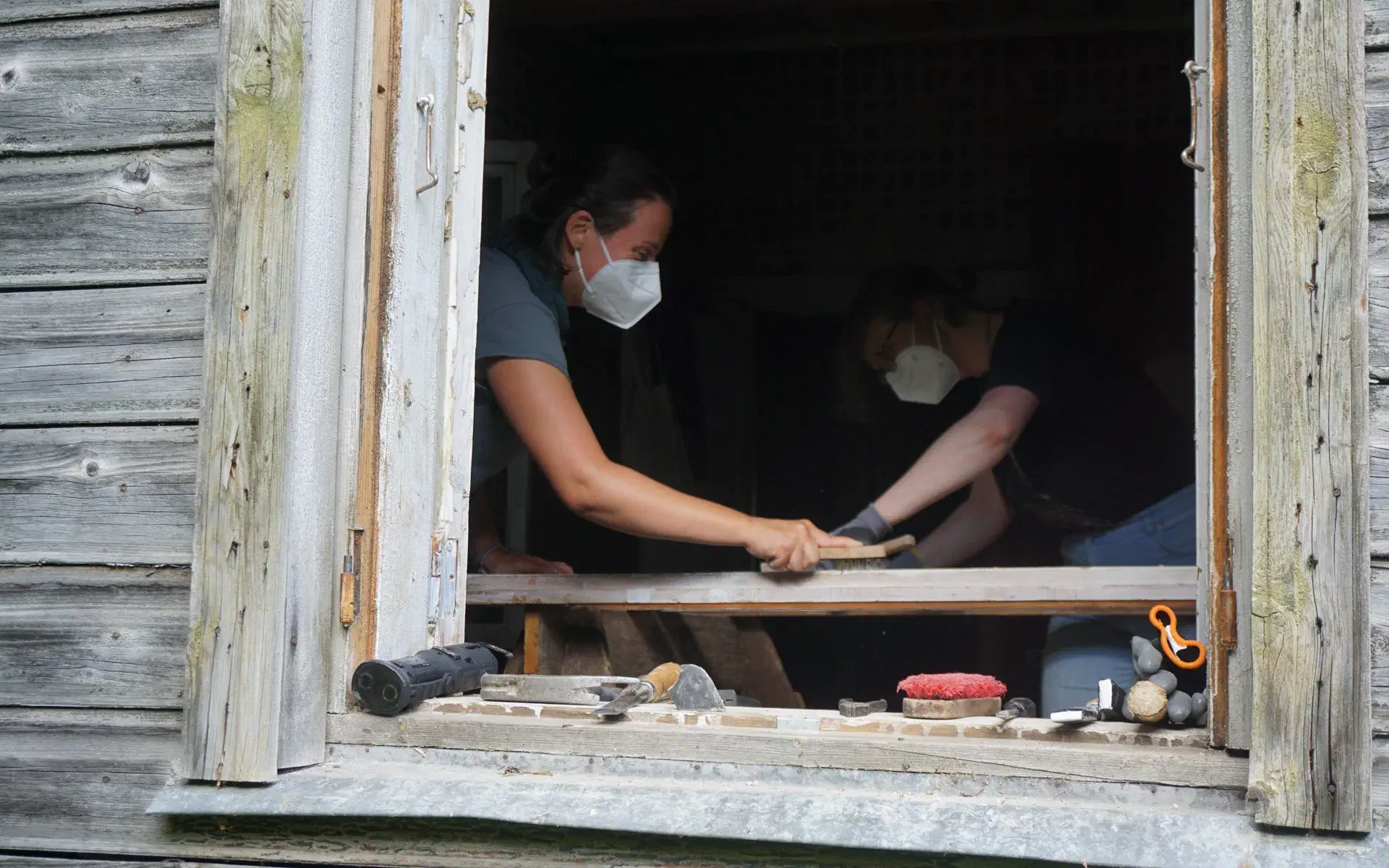 Anna scrubs window frames with a wire brush.