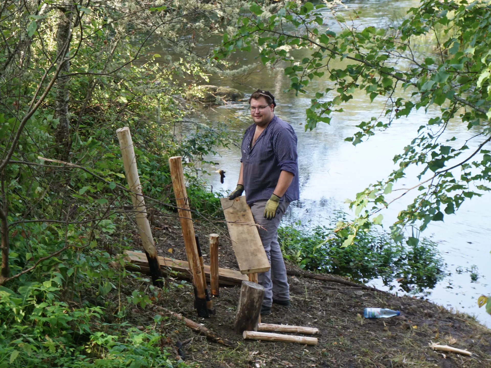 Sören legt das Sitzbrett auf die Bankpfähle auf. Im Hintergrund der Kunda-Fluss