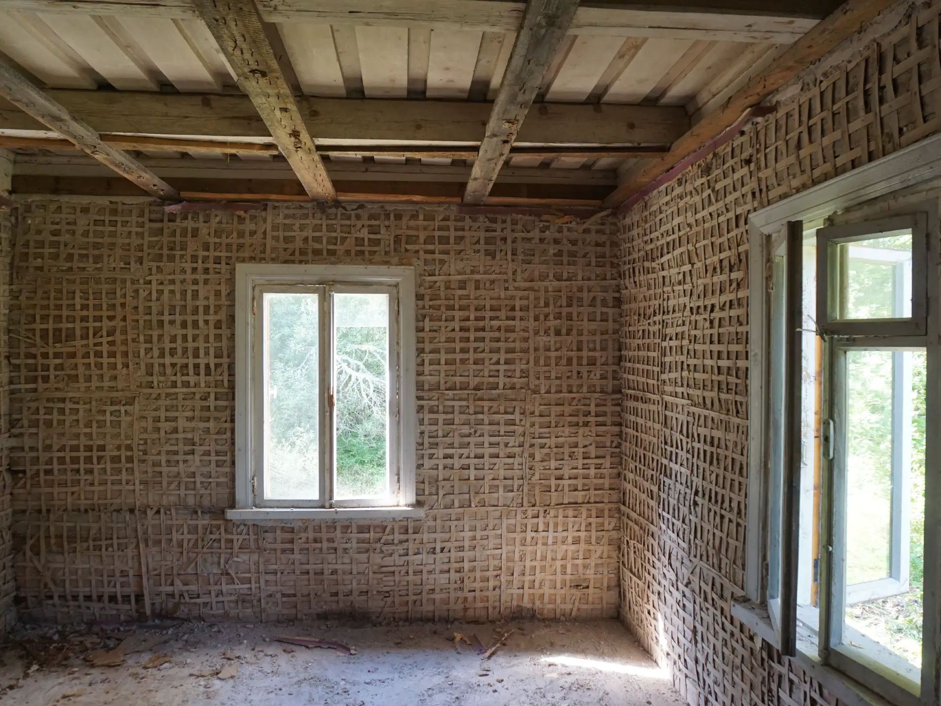 Nach dem Putz entfernen kommt auf dem Holz in Blockbauweise ein feines Gitter aus Holzstreifen zum Vorschein. An der Decke sind wieder Deckenbalken zu sehen