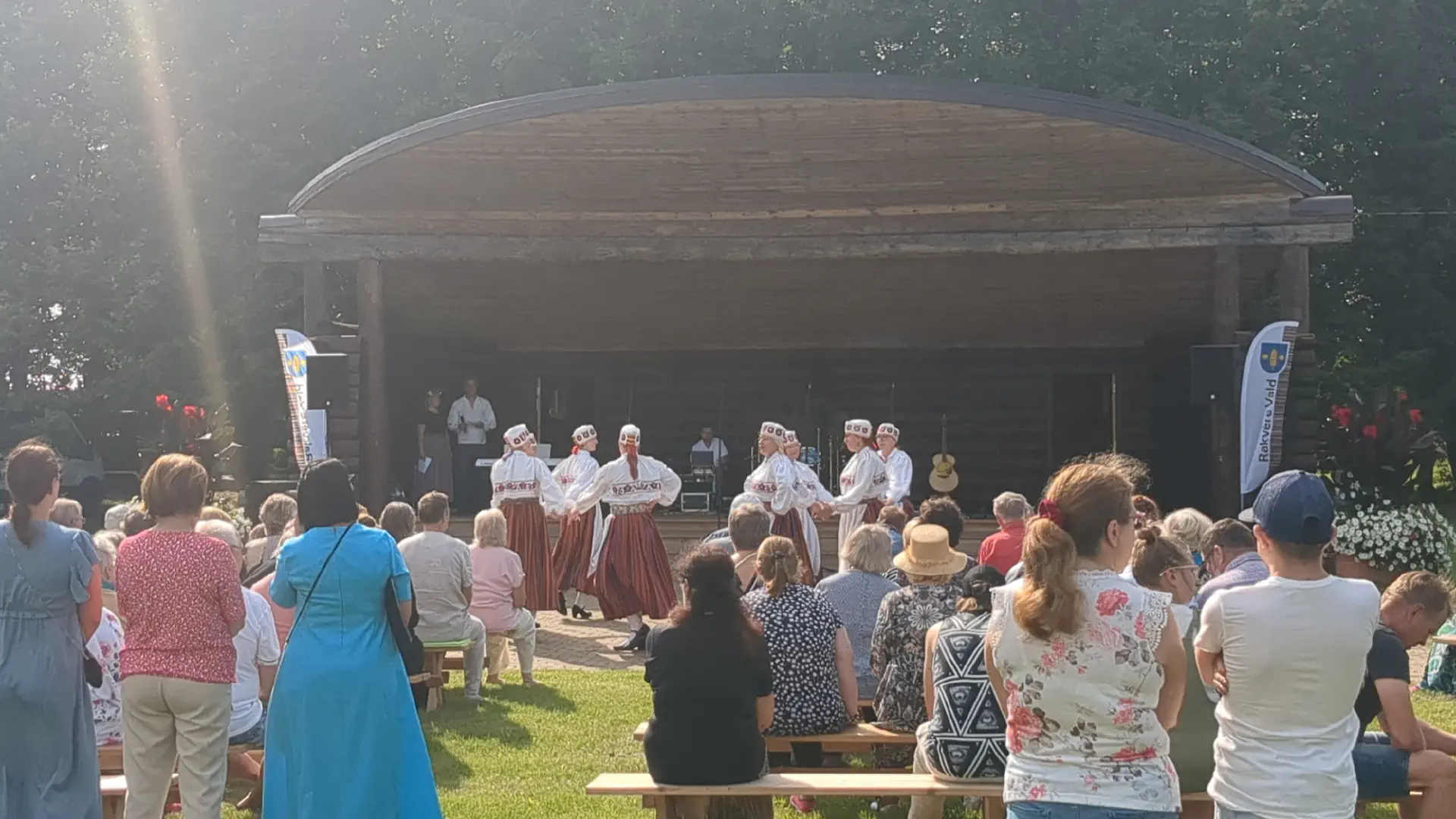 Women in traditional Estonian costumes dance in front of a large wooden stage