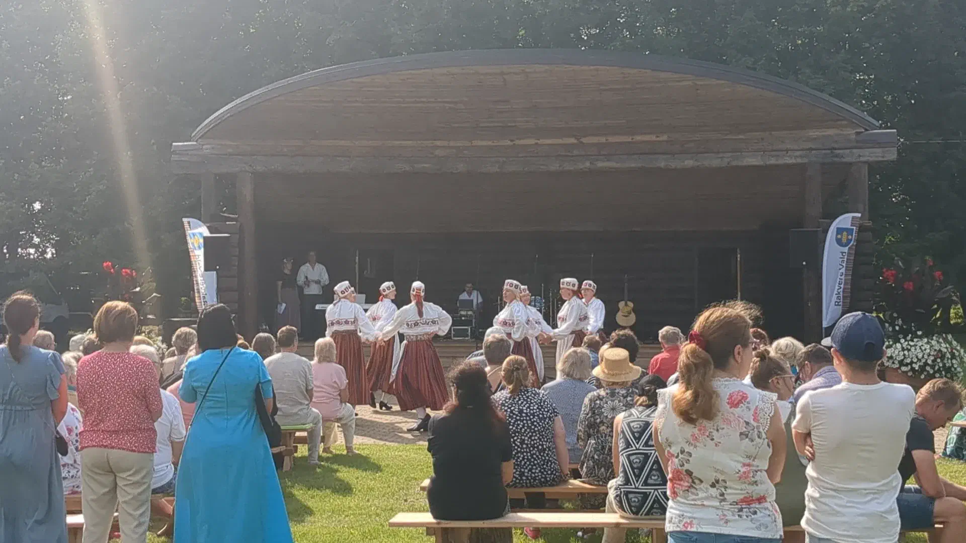 Women in traditional Estonian costumes dance in front of a large wooden stage