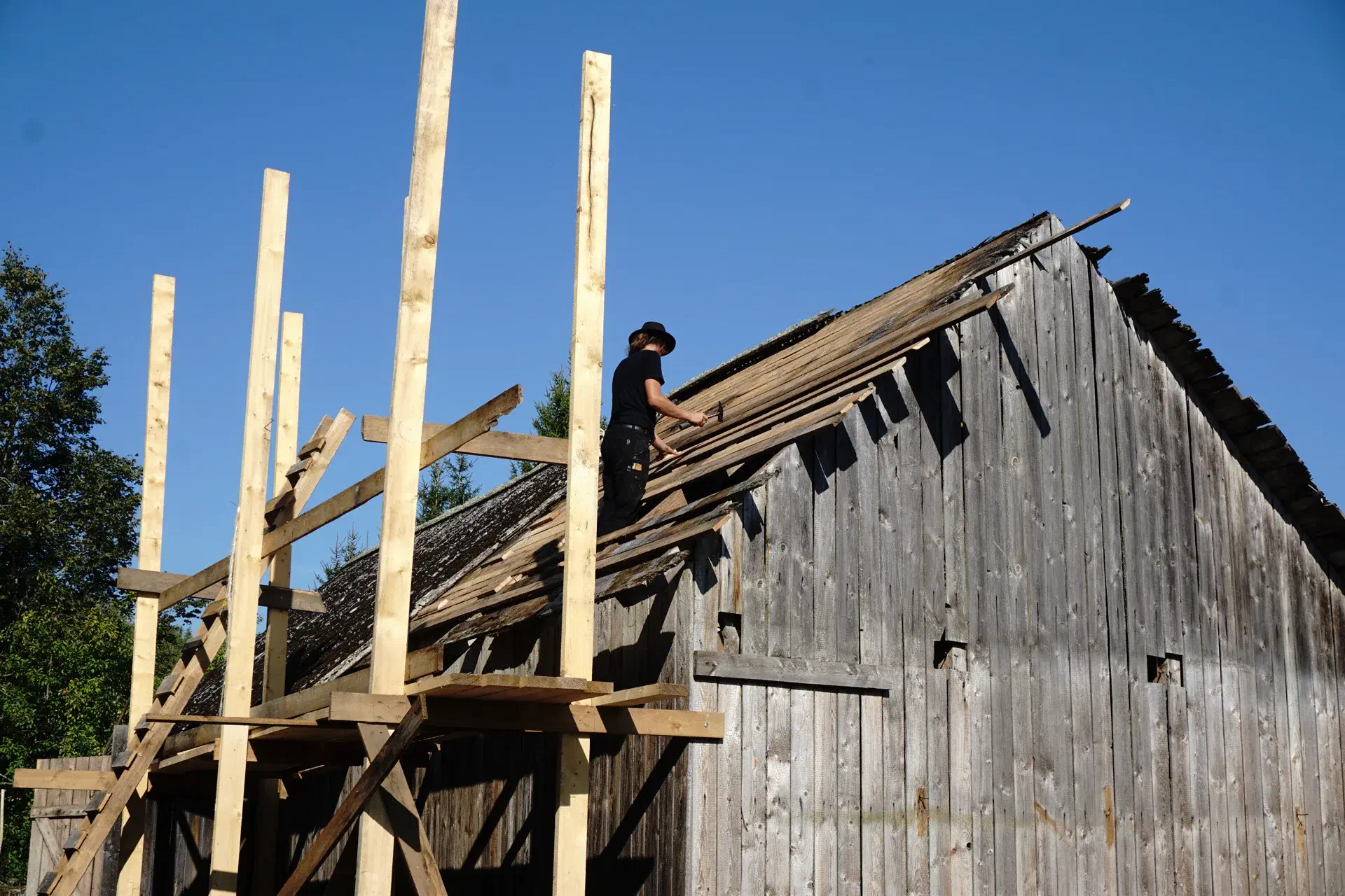 Jacob stands on the half-covered barn roof. Wooden scaffolding in the foreground