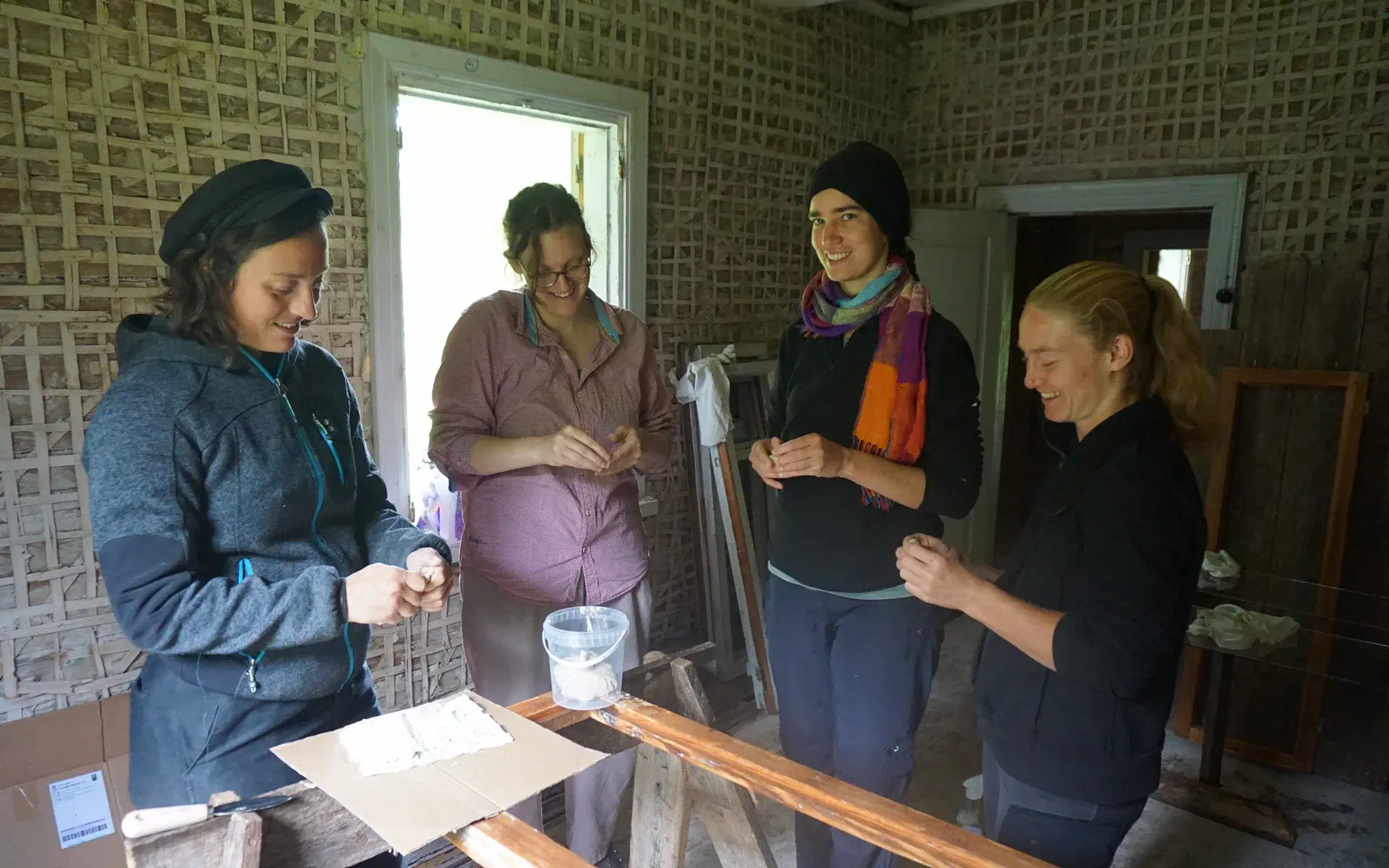 Four people are standing around a window frame, kneading putty between their fingers.