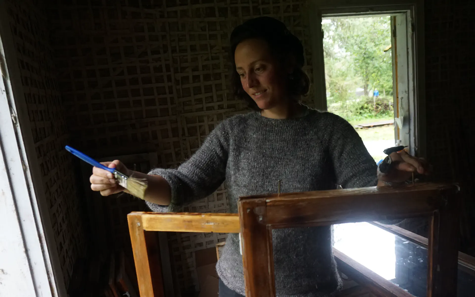 Anna trägt mit einem Pinsel Leinöl auf einen geschliffenen Fensterrahmen auf.