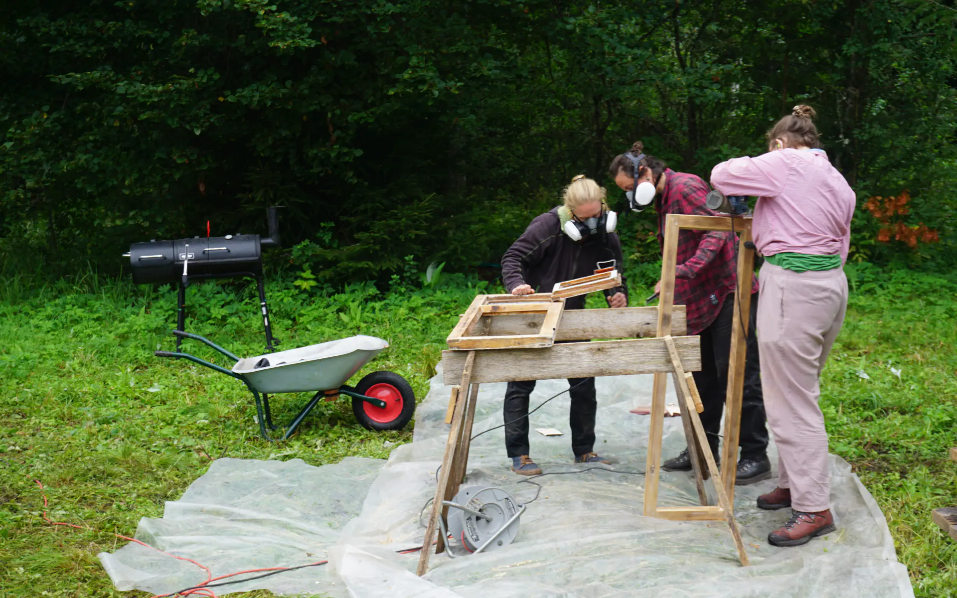 Drei Menschen schleifen zwei Fensterflügel im Freien.