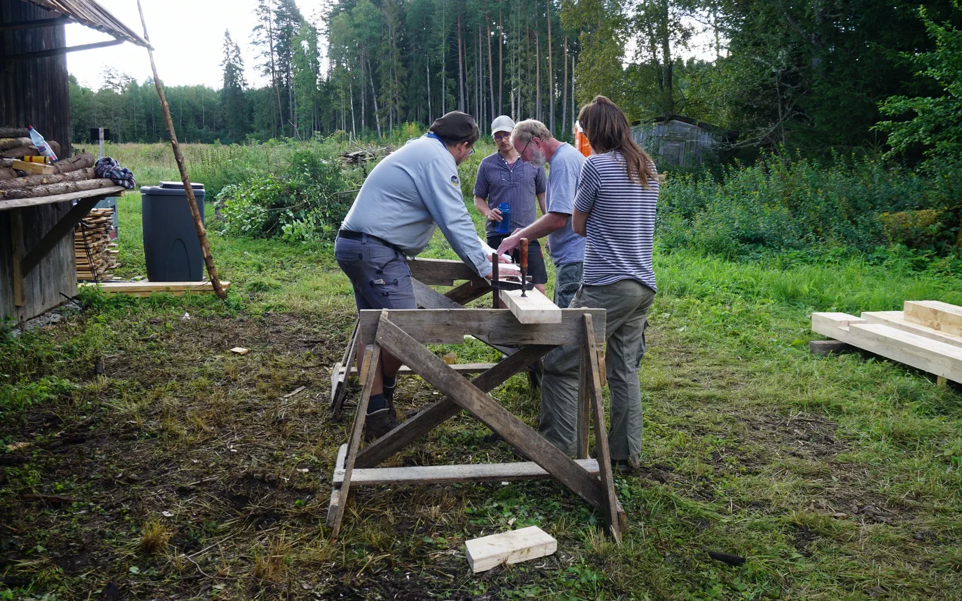Four people are standing at two trestles and cutting beams.