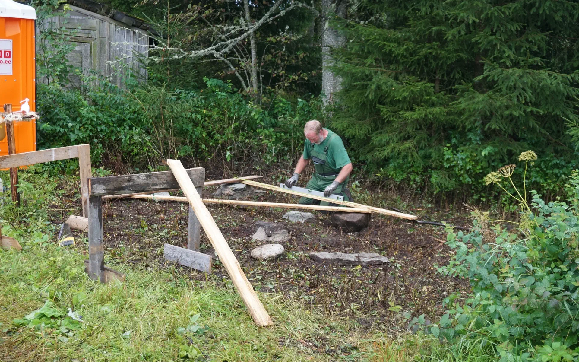 Tobias kneels on the floor and uses a level to align the stones that form the foundation.