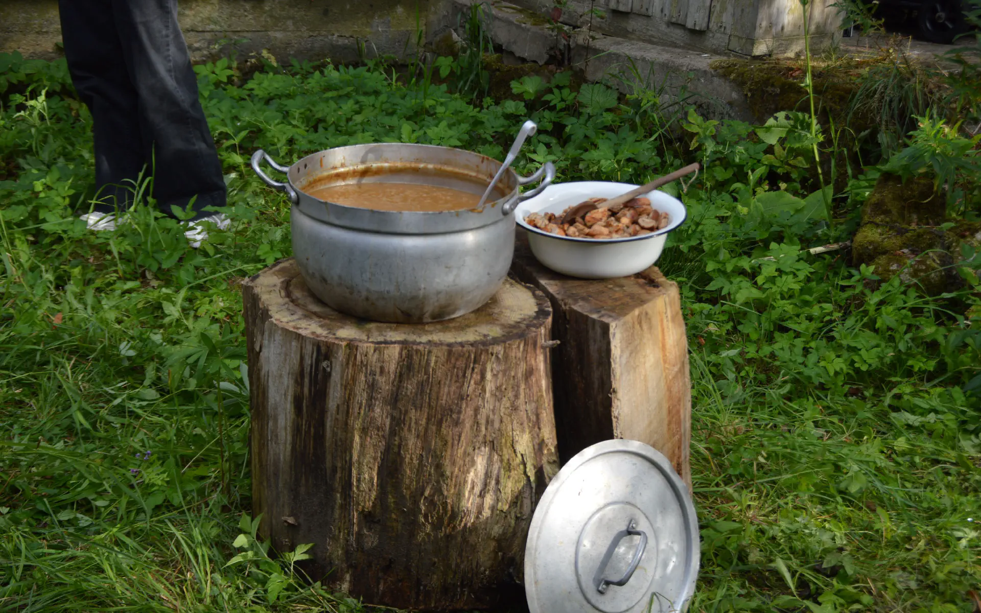 Ein Topf Zwiebelsuppe steht neben einer Schale Croutons auf zwei Holzstümpfen