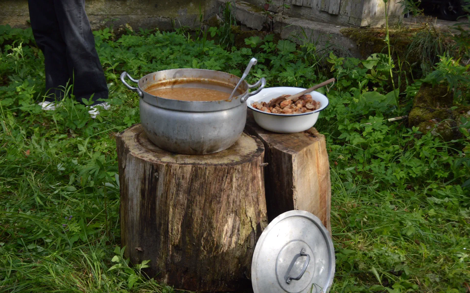 A pot of onion soup stands next to a bowl of croutons on two wooden stumps.