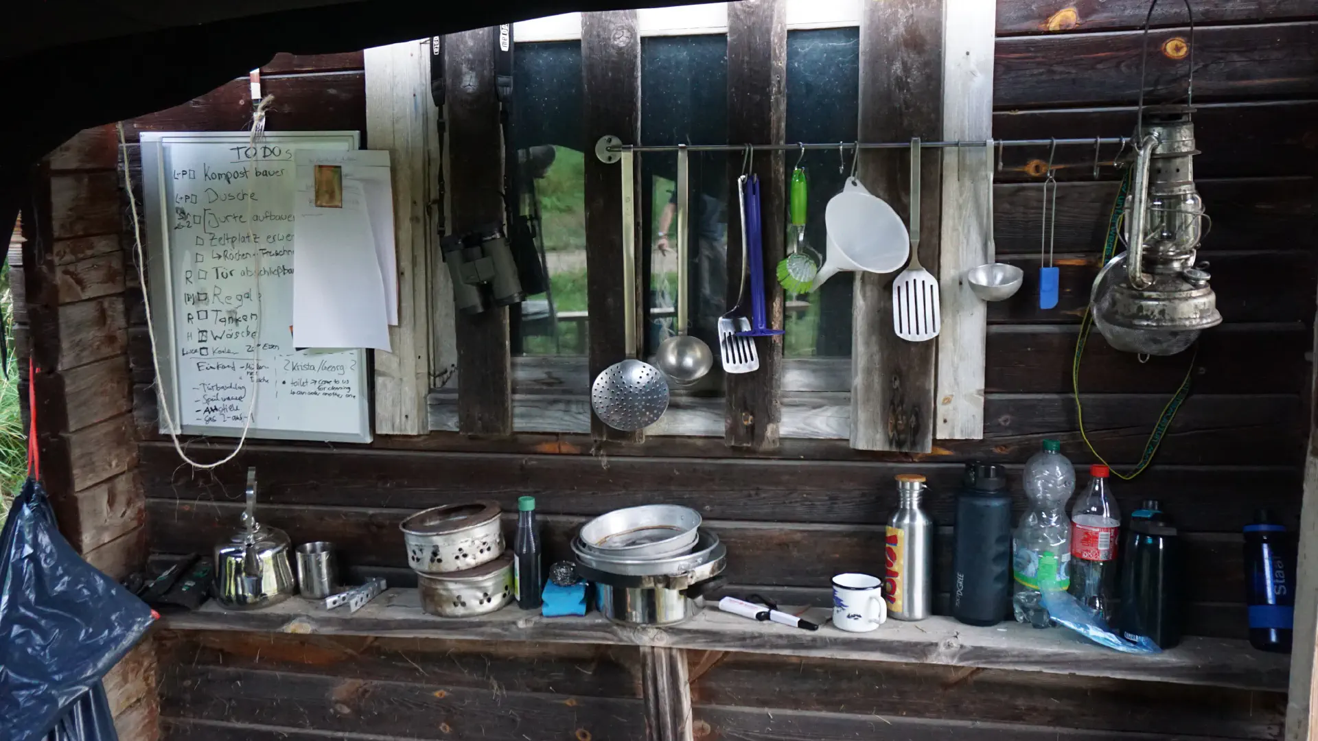 Various kitchen utensils, a funnel and an oil lamp hang from a horizontal bar screwed to the old sauna house