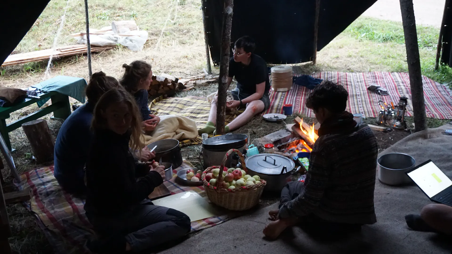 Five people sit on rugs in the yurt. A basket of apples in the foreground