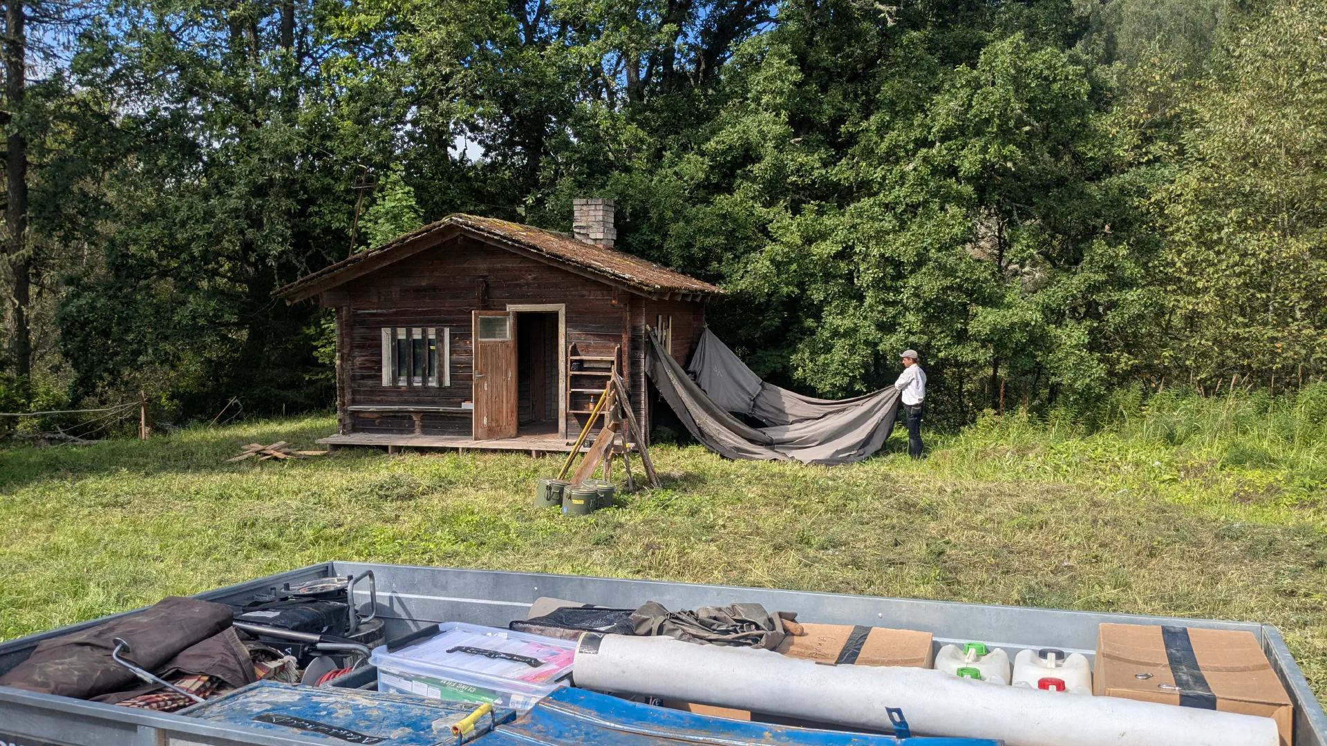 Anton sets up the tent next to the sauna. Trailer with luggage in the foreground.