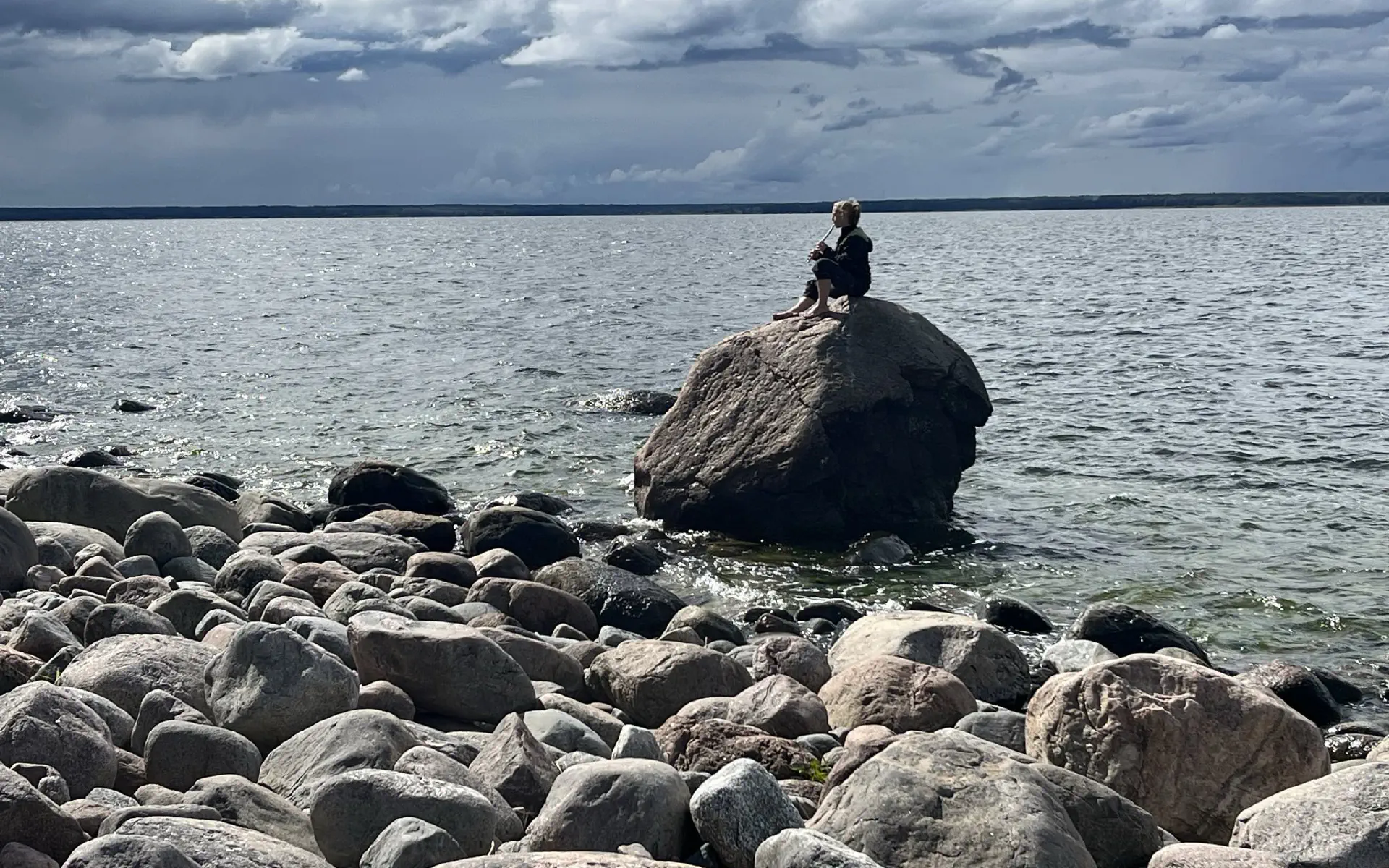 Petra sitzt auf einem großen Stein in der Ostsee und spielt auf ihrer Flöte