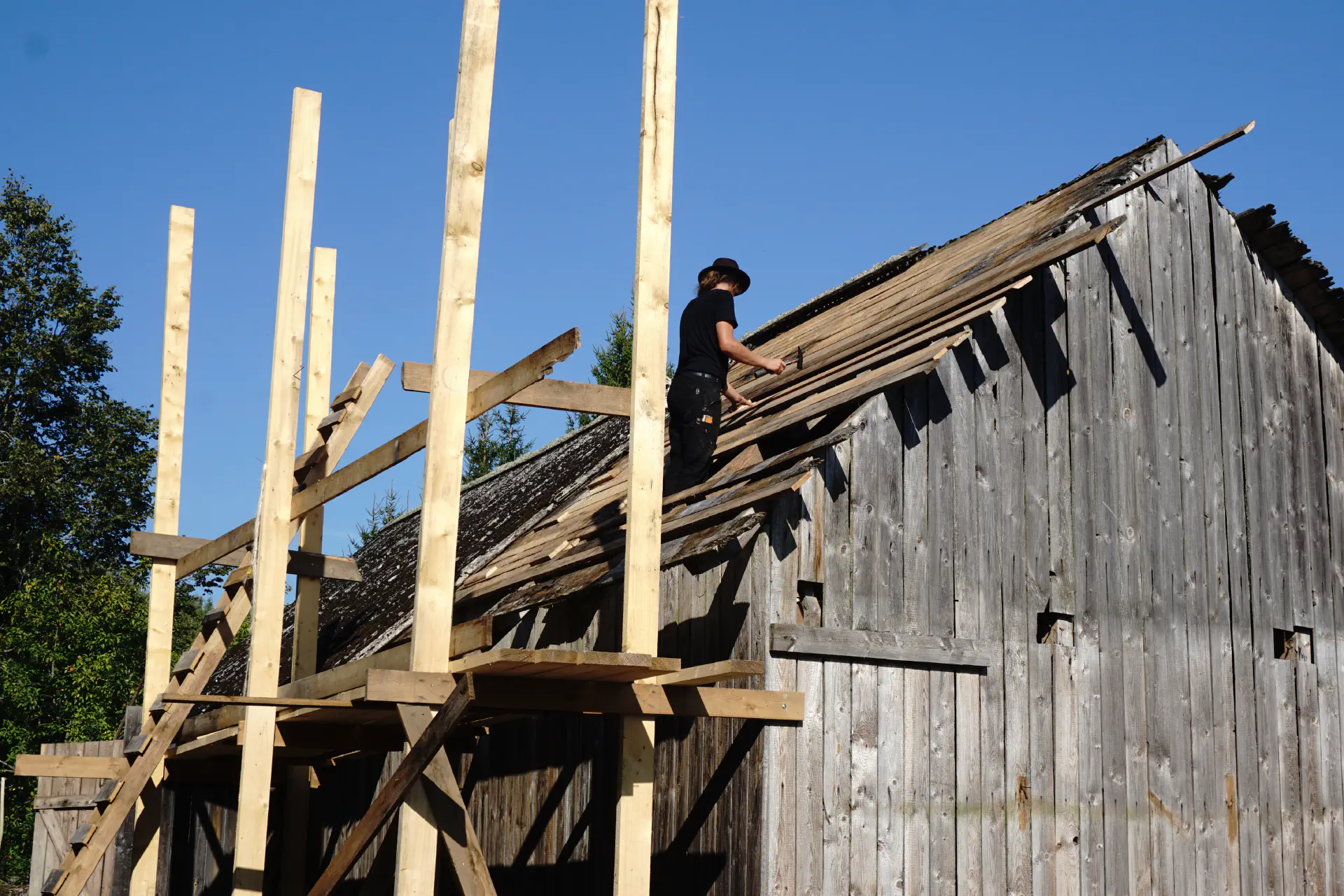 Jacob stands on the half-covered barn roof. Wooden scaffolding in the foreground